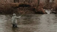 Muž stojící v řece s rybářským prutem při nahození